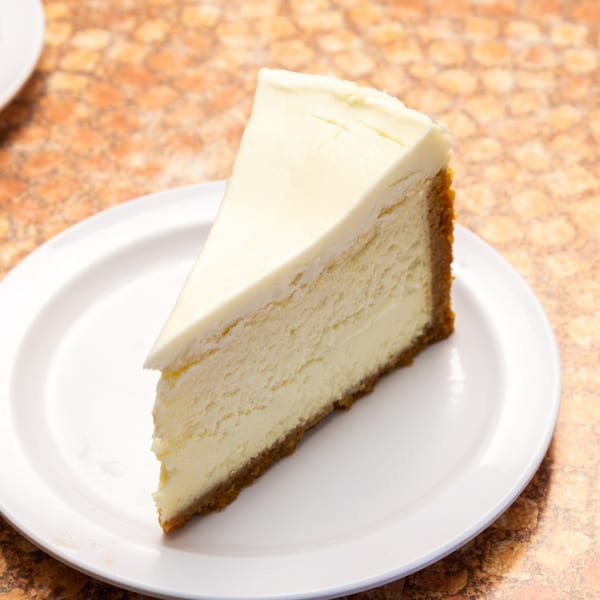 A slice of classic New York cheesecake with a graham cracker crust on a white plate.