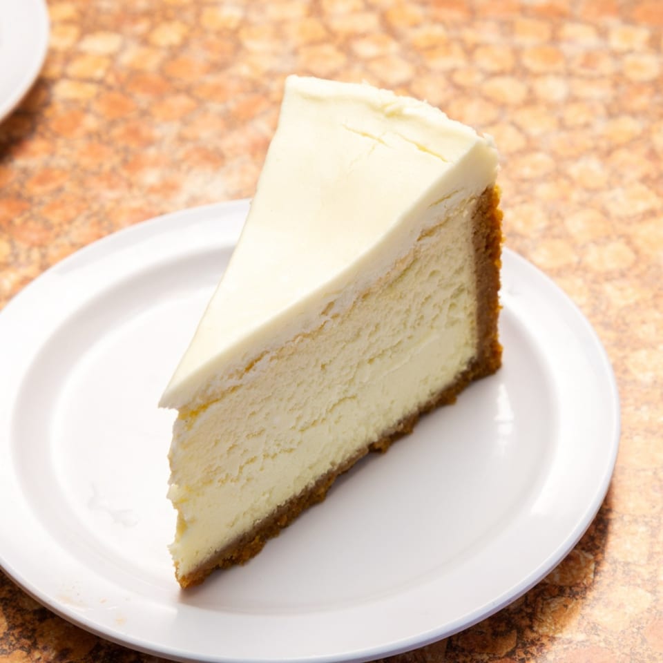 A slice of classic New York cheesecake with a graham cracker crust on a white plate.