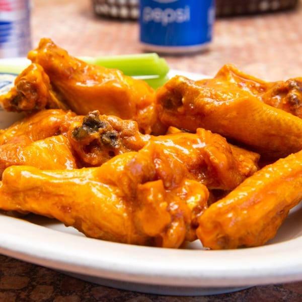 A plate of Brooklyn Joe's spicy buffalo wings with celery sticks and a Pepsi can in the background.